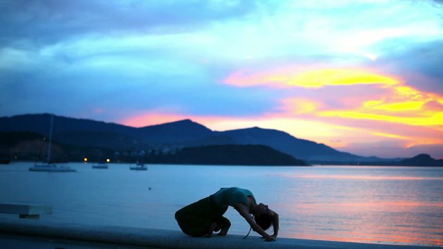 Young woman doing yoga bridge, sunset silhouette on island