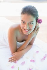 Obraz na płótnie Canvas Smiling brunette lying on towel with rose petals