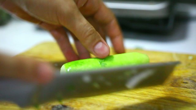 female hands chopping cucumber on a wooden board