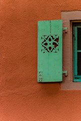 Orange stone wall with green ornamented shutter.