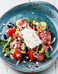 Greek salad with feta cheese and sun-dried olives on blue backgr