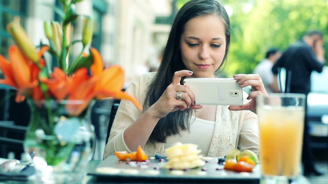 Woman taking photo of tasty dessert with cellphone in cafe