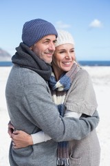 Attractive couple hugging on the beach in warm clothing