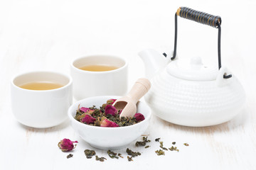 green tea with rosebuds, cups and teapot on white wooden table