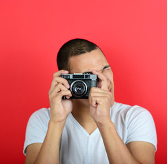 Portrait of young male holding vintage camera against red backgr