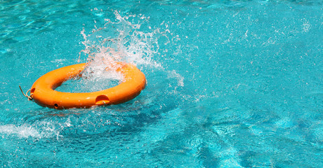 Orange life buoy splash water in the blue swimming pool