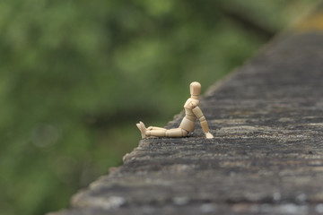 EntspannungEine Holzgliederpuppe sitzt auf einer alten Steinmauer in Augsburg und blickz nach links in einen unscharfen Hintergrund