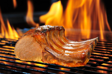 Grilled pork chop on the flaming grill.