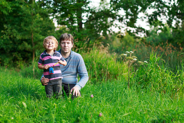 Fototapeta premium Little boy and his father sitting on grass in summer forest