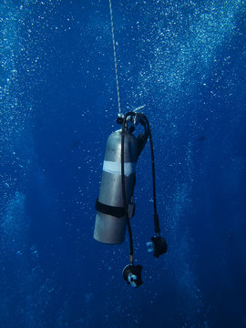 Stage tank and regulator rigged on a decompression line in clear blue ocean water for scuba diving safety.