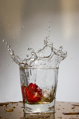 Strawberry falls with a splash in a glass with water.