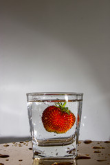 Strawberry falls with a splash in a glass with water.