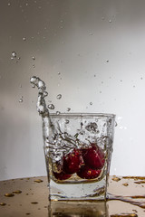 Cherry falls with a splash in a glass with water.