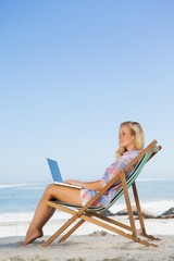 Pretty blonde sitting on beach using her laptop