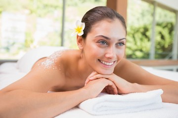 Obraz na płótnie Canvas Beautiful smiling brunette lying on massage table with salt scru
