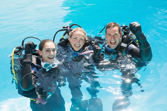 Smiling friends on scuba training in swimming pool cheering at c