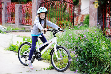 Fototapeta premium Adorable kid girl in blue helmet riding her bike 
