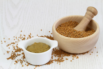 Mustard seeds in wooden mortar and mustard in white bowl