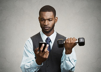 Businessman reading text message on mobile lifting weight simult