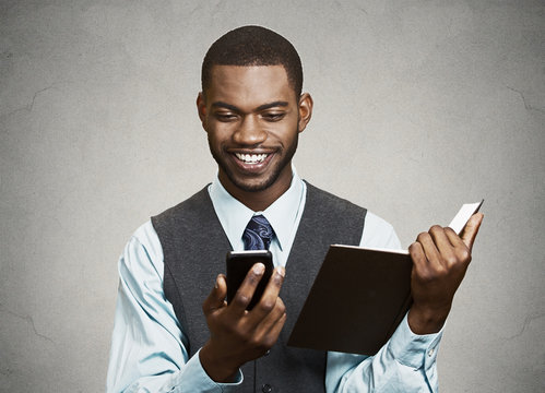 Businessman reading text message on mobile holding book simultan