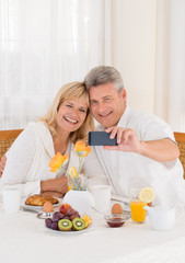 Obraz na płótnie Canvas Happy mature couple take selfie photo at healthy breakfast