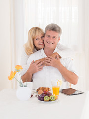 Obraz na płótnie Canvas Romantic happy mature couple with smiles hugging on breakfast