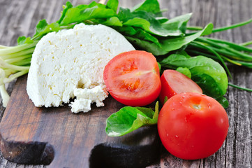 Cheese with tomatoes and arugula and onion on a wooden board