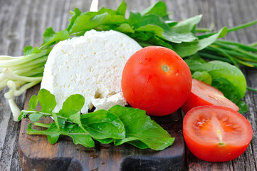 Cheese with tomatoes and arugula and onion on a wooden board