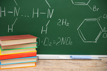 Pile of books against a school board with chemical formulas.