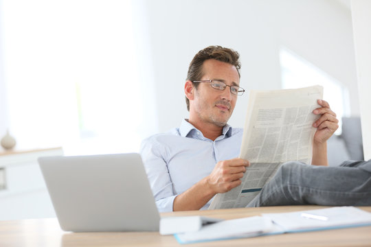 Man reading newspaper with stretched legs over table