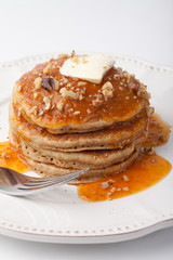 Wholesome homemade whole wheat pancakes with an apricot sauce topped with butter and chopped walnuts on a white background
