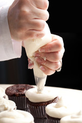 Chef decorating and piping buttercream icing on chocolate filled chocolate cupcakes