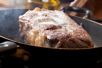 Searing of an organic grass fed cross rib roast with steam coming off of it and a bottle of olive...