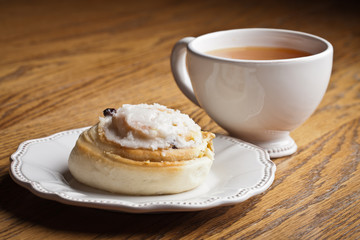 Macro shot of a cinnamon roll on an antique dish next to a cup of hot wassail on a wooden table