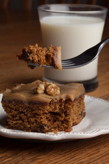 Macro shot of carrot cake topped with a walnut with a bite on a fork next to a glass of cold milk