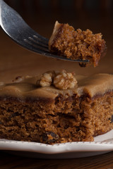 Macro shot of carrot cake topped with a walnut with a bite suspended on a fork