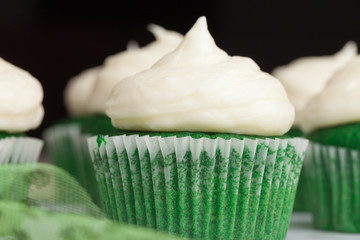 Macro shot of St. Patrick's Day green velvet cupcakes piped with a decadent cream cheese frosting -...