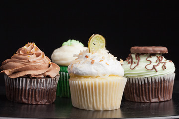 Side view of Coconut Key Lime Cupcake, Pot of Gold Chocolate Caramel Cupcake, Irish Mint Chocolate Cupcake, and Green Velvet Cupcake topped with cream cheese frosting