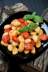 Glass plate with roasted gnocchi and tomatoes on wooden logs