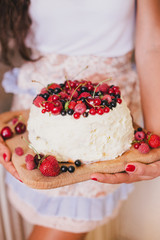 Cake with fresh berries and white glaze in woman's hands