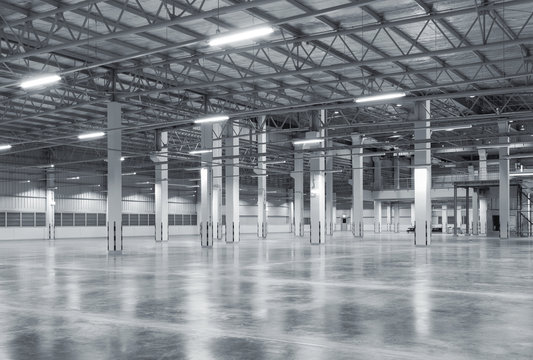 Spacious modern warehouse with polished concrete floor, structural columns and illuminated roof trusses, offering copy space for logistics, distribution, manufacturing and industrial real estate.