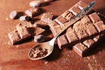 Cocoa powder and dark chocolate on color wooden background
