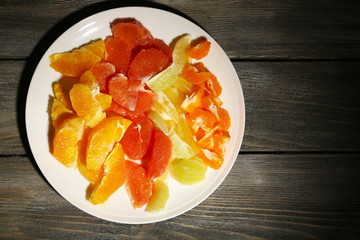 Sliced citrus fruits on plate, on wooden background