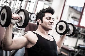 Young man exercising with dumbbells in a gym. Filtered image.