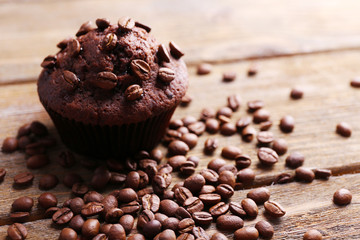 Chocolate muffin and coffee grains on wooden background