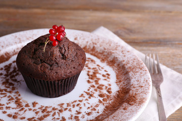 Chocolate muffin with red currant on plate on wooden background