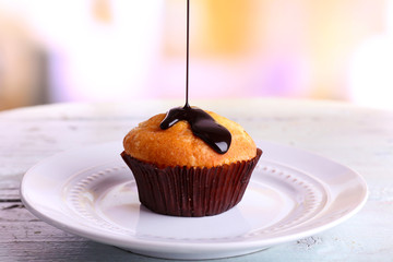 Tasty muffin with chocolate sauce on plate, on bright