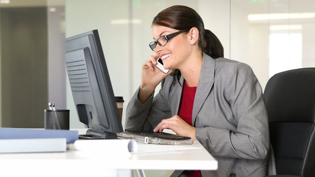 Young businesswoman talking on phone at desk with computer