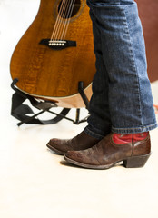 Legs of country musician in boots in front of guitar
