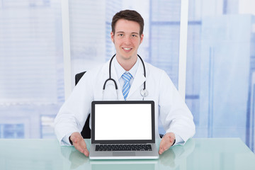 Doctor Presenting Laptop With Blank Screen At Desk